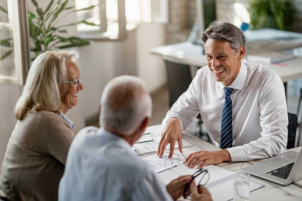 Smiling older adults reviewing documents together at a kitchen table with coffee and sunlight.